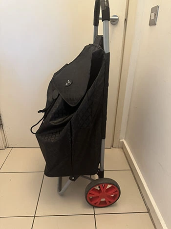 Black personal shopping trolley from the side, highlighting its medium-sized red wheels